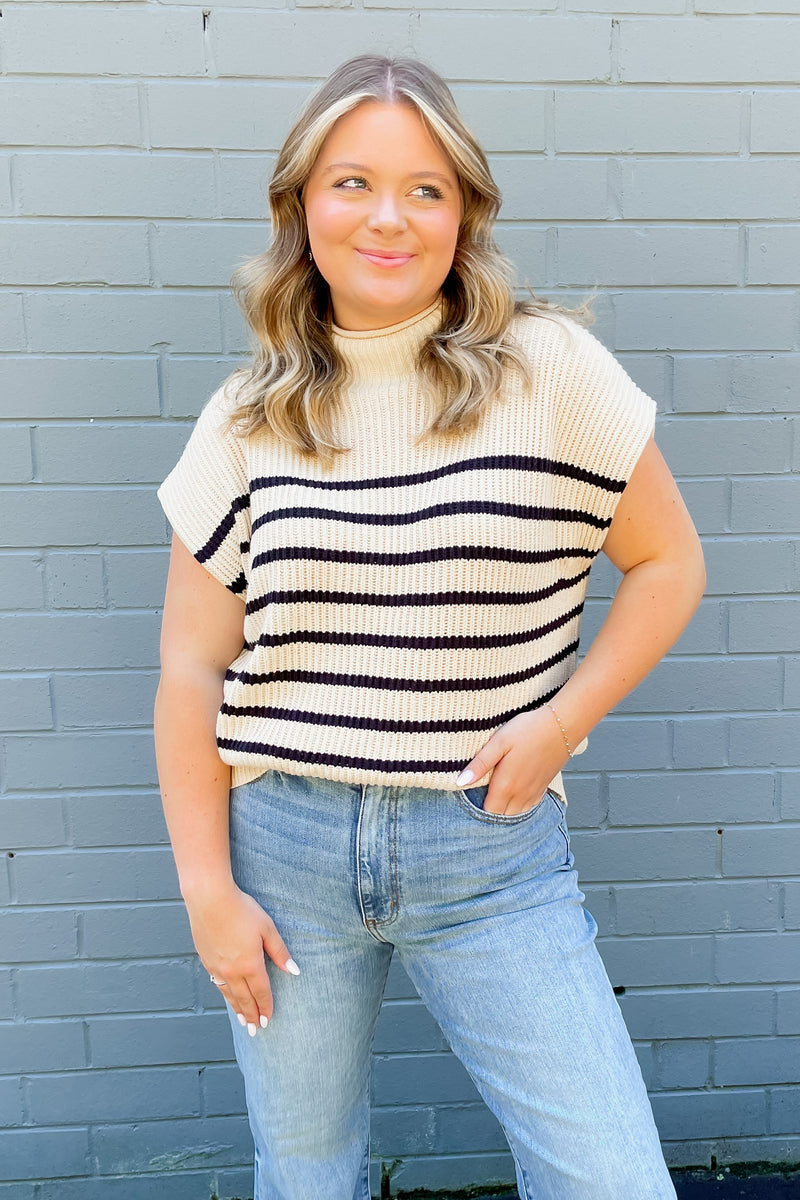 Cream colored sleeveless, mock neck sweater with stripes.