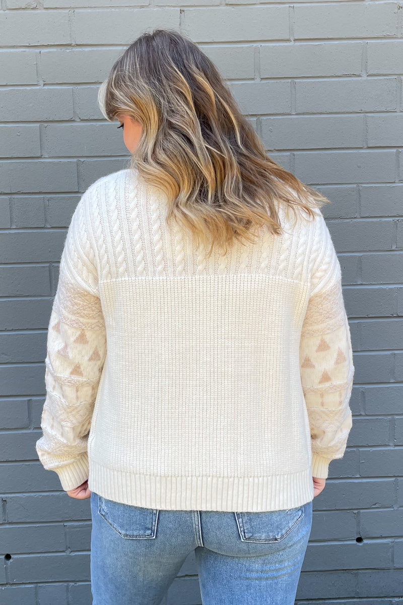 Long sleeve cream sweater with cable knit detailing and tortoise buttons. Abstract fall print on the sleeves.
